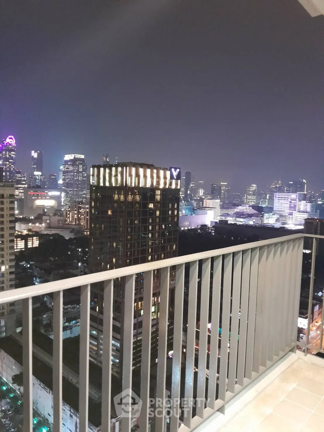 Stunning cityscape view from a high-rise balcony at night, showcasing vibrant urban lights.