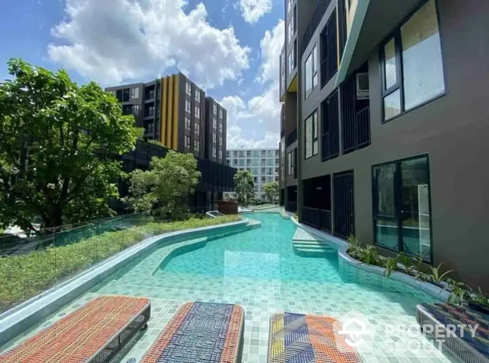 Modern apartment complex with stunning pool and lush greenery under a bright blue sky.