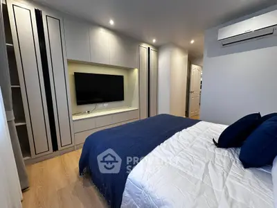 Modern bedroom with built-in wardrobe and wall-mounted TV, featuring cozy bedding and sleek air conditioning unit.