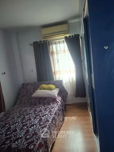 Cozy bedroom with patterned bedspread and natural light through window.