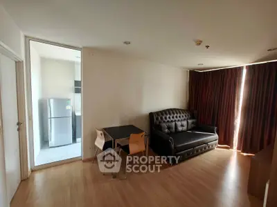 Modern living room with stylish sofa and dining area, adjacent to a kitchen with a fridge.