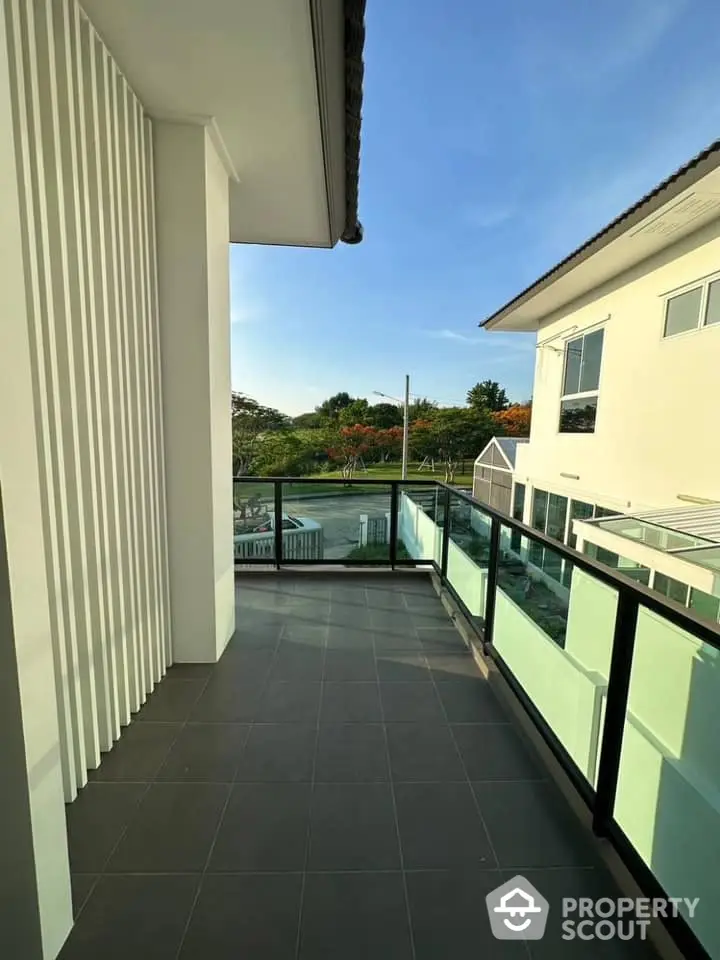 Spacious balcony with modern glass railing offering a serene view of lush greenery, perfect for outdoor relaxation and entertainment.