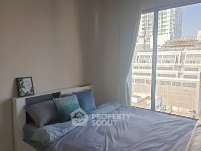 Modern bedroom with large window and city view, featuring stylish bedding and decor.