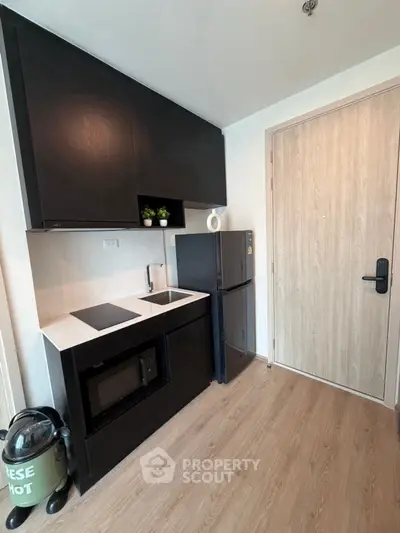 Modern compact kitchen with sleek black cabinets and appliances, featuring a microwave and mini fridge.
