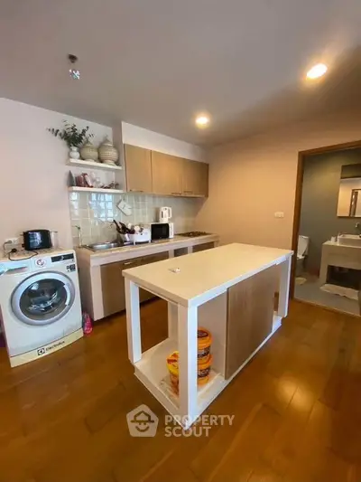 Modern kitchen with island and washing machine, featuring wooden flooring and sleek cabinetry.