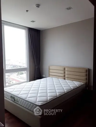 Spacious bedroom with large window and modern decor in high-rise apartment.