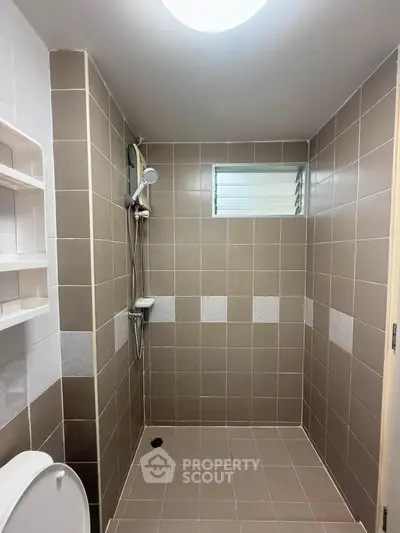 Modern bathroom with tiled shower area and small window for ventilation.