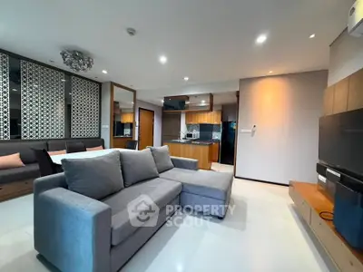 Modern living room with stylish decor and open kitchen layout, featuring a cozy gray sofa and sleek wooden accents.