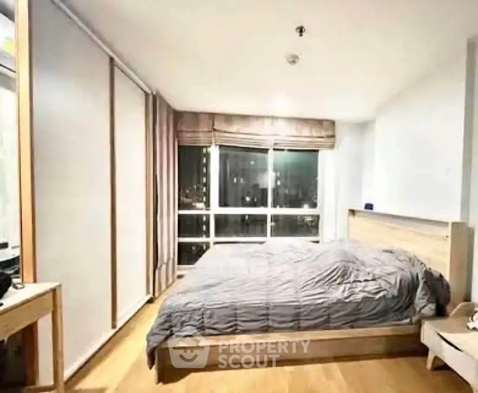 Spacious bedroom with large window offering stunning city views, featuring modern furnishings and ample natural light.