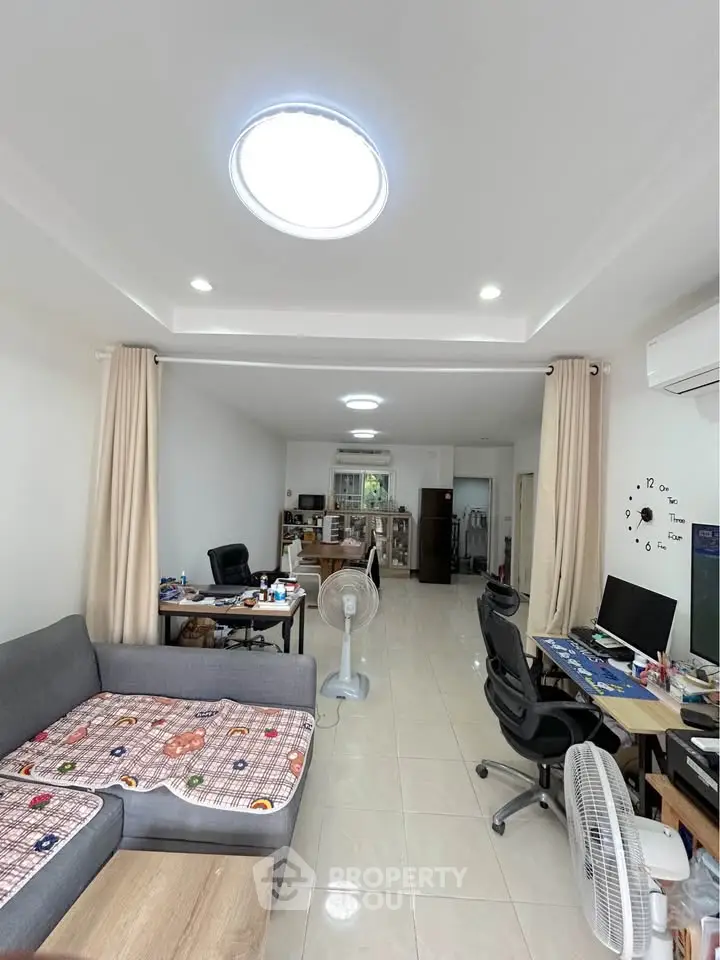 Spacious living room with modern decor and ample natural light, featuring a cozy seating area and workspaces.