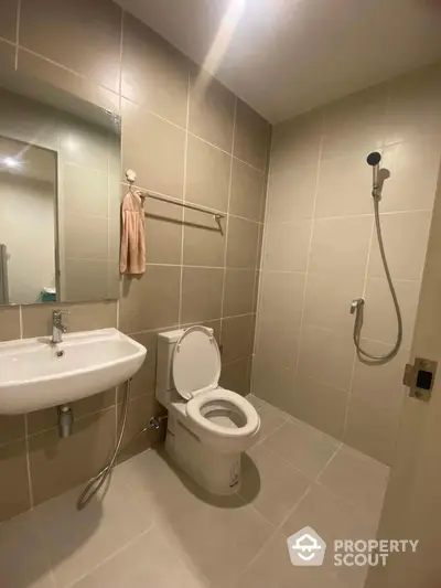 Modern bathroom with sleek fixtures and neutral tiles, featuring a shower and toilet.