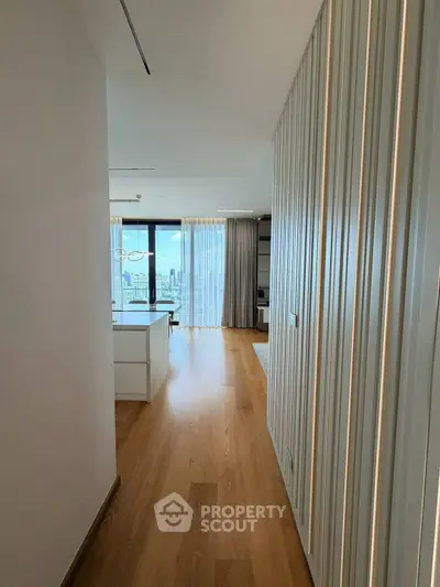 Modern apartment hallway leading to a bright living room with city view.