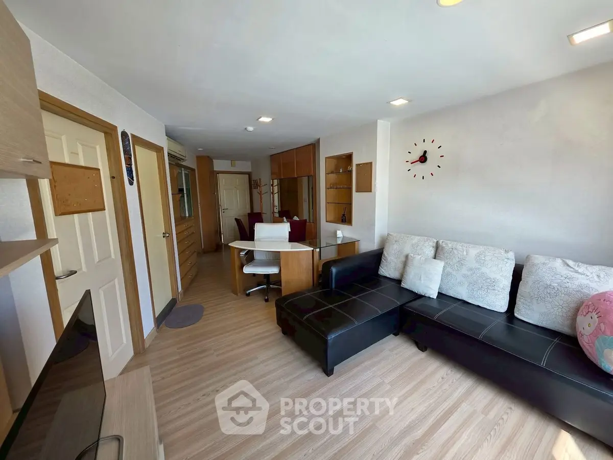 Modern living room with sleek black sofa and wall clock, featuring open layout and wooden flooring.