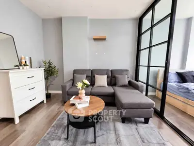 Modern living room with stylish gray sofa and glass partition leading to bedroom