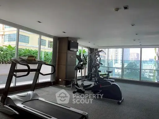 Spacious gym with modern equipment and large windows offering city views.