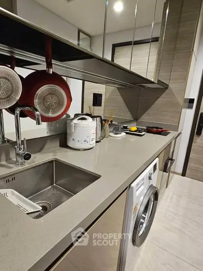Modern kitchen with sleek countertops, washing machine, and hanging cookware in a stylish apartment.