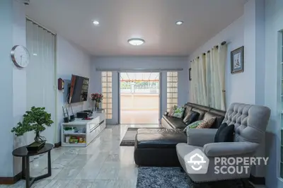 Spacious living room with gleaming tiled floors, modern furnishings, and abundant natural light streaming through large glass doors leading to a cozy balcony.