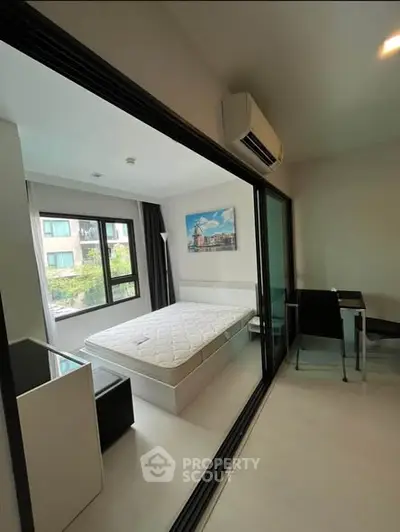 Modern bedroom with glass partition and air conditioning, featuring a minimalist design and natural light.