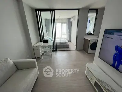 Modern living room with sleek design and glass partition leading to a cozy bedroom.