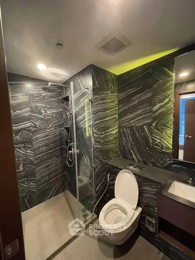 Luxurious modern bathroom with sleek black marble tiles and glass shower enclosure.