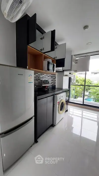 Modern kitchen with sleek cabinets, washing machine, and large window view.