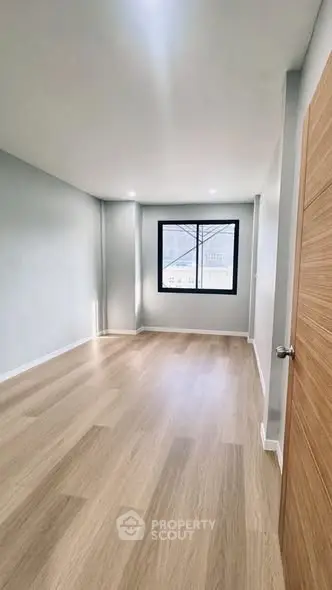 Spacious empty room with wooden flooring and large window, perfect for customization.