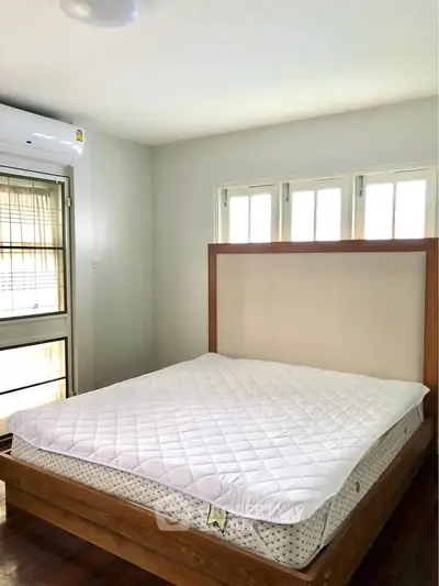 Spacious bedroom with large windows and modern air conditioning unit, featuring a comfortable wooden bed frame.