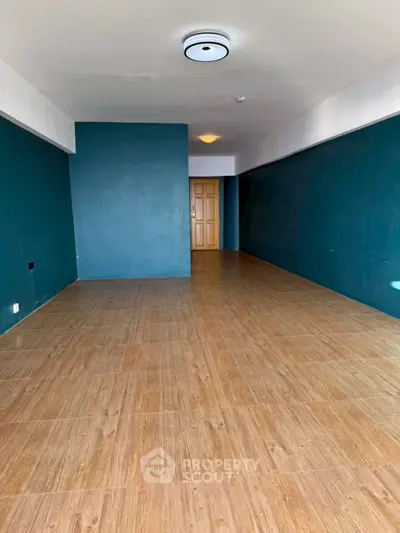 Spacious empty room with wooden flooring and teal accent walls, ideal for customization.