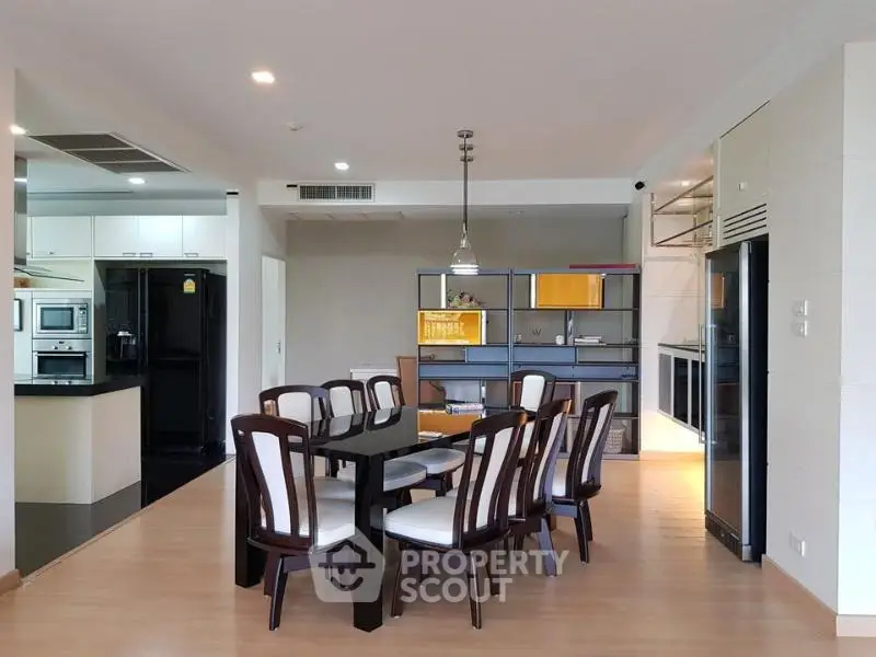 Spacious dining area with modern kitchen and elegant wooden furniture in open layout apartment.