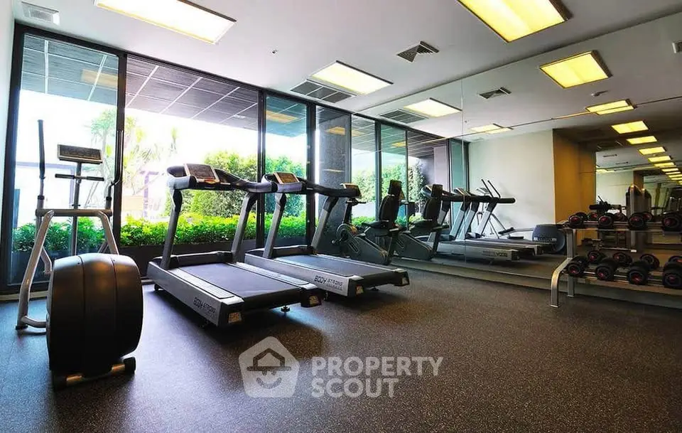 Modern gym with treadmills and weights, large windows offering lush garden views.