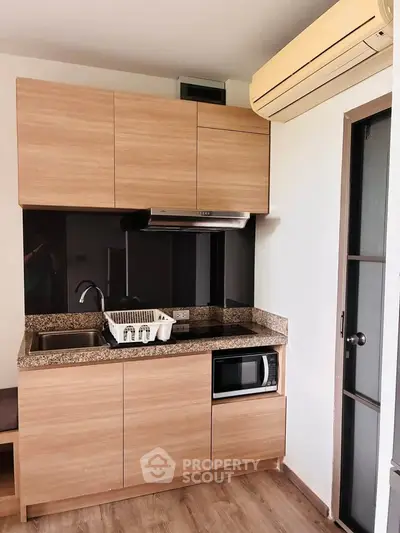 Modern compact kitchen with wooden cabinets, granite countertop, and built-in microwave in a cozy apartment.