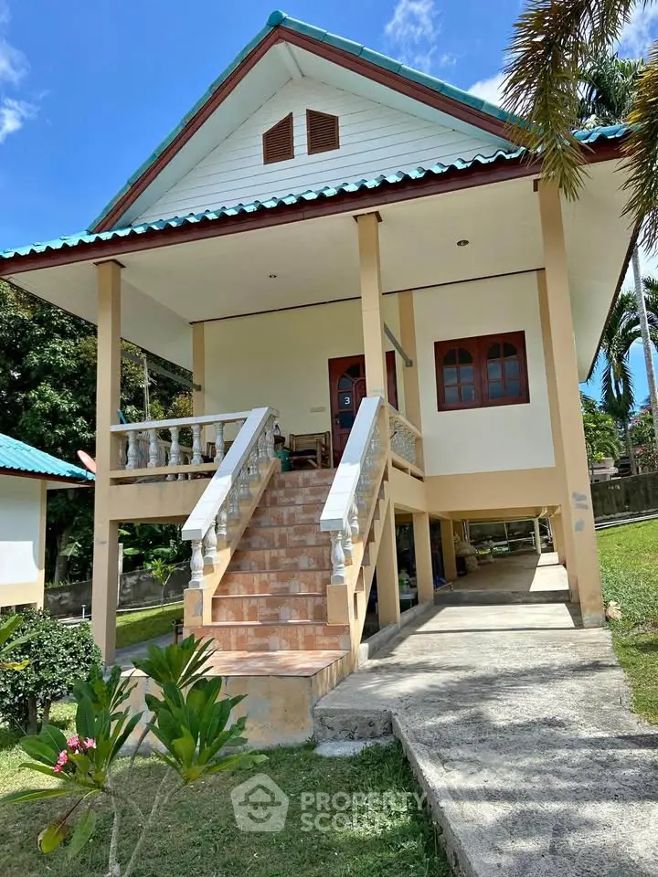 Charming elevated house with front staircase and lush garden, perfect for tropical living.