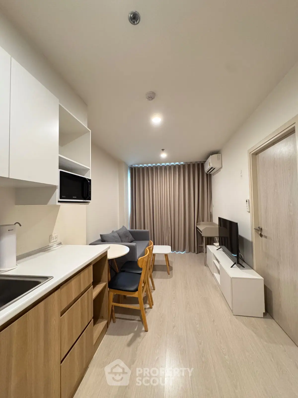 Modern compact living room with open kitchen, featuring sleek furniture and natural light.