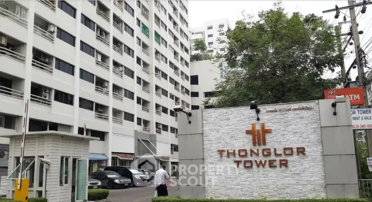 Modern high-rise building exterior with Thonglor Tower signage and lush greenery.