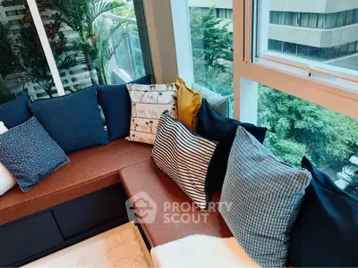 Stylish corner seating area with plush cushions and large windows offering lush greenery views.