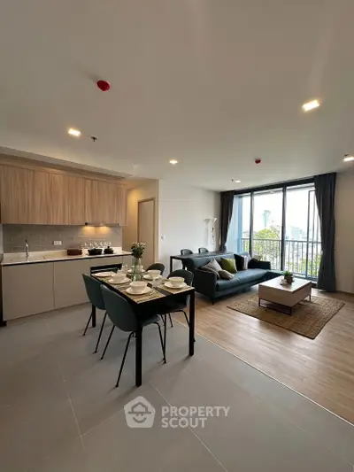 Modern open-plan living room with kitchen, stylish furniture, and large windows offering natural light.