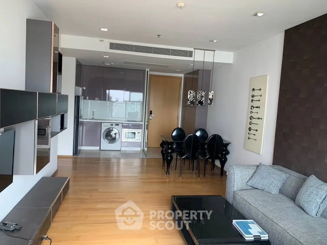 Modern living room with open kitchen, sleek furniture, and hardwood floors in a contemporary apartment.