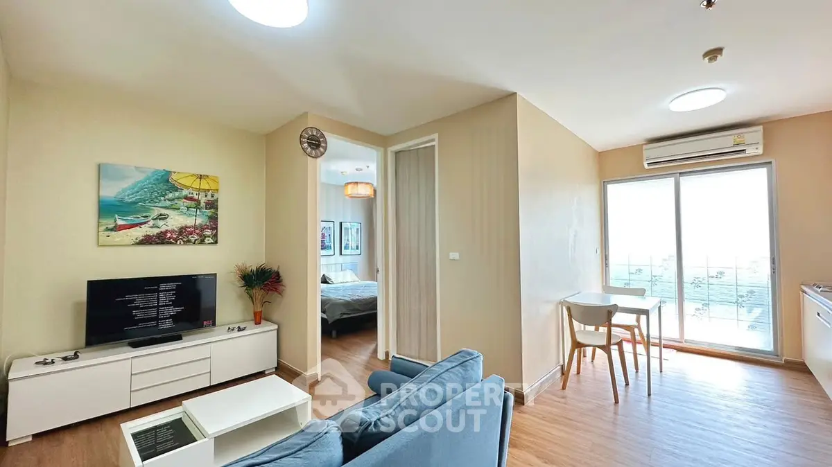 Modern living room with cozy seating, TV, and dining area in a bright apartment with balcony access.