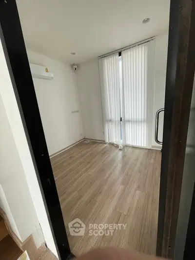Spacious empty room with wooden flooring and vertical blinds, perfect for customization.