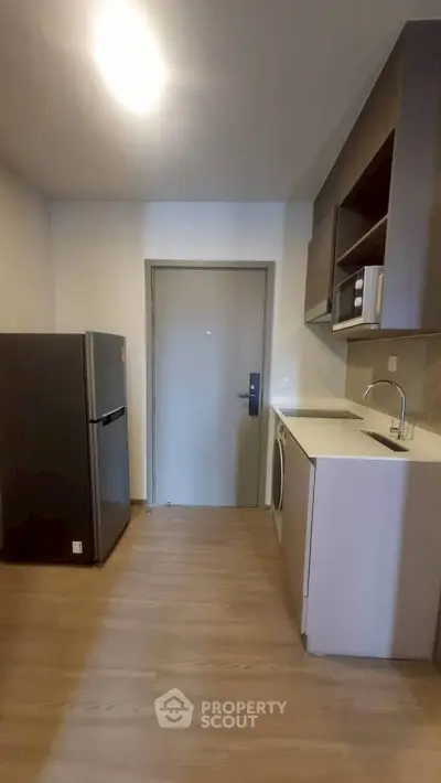 Modern compact kitchen with fridge, washing machine, and microwave in sleek apartment.