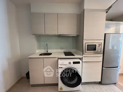 Modern compact kitchen with washing machine, microwave, and fridge in sleek apartment.