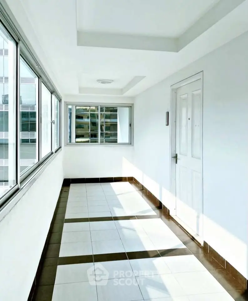 Bright corridor with large windows in modern building, offering ample natural light and sleek tiled flooring.