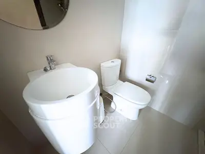 Modern bathroom with sleek fixtures and minimalist design, featuring a compact sink and toilet.