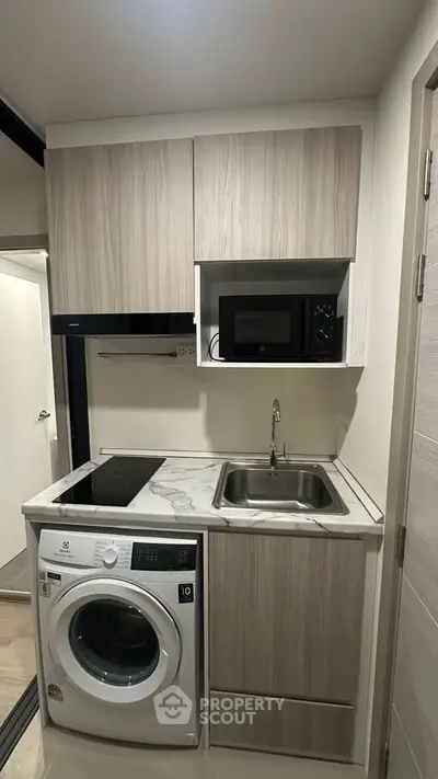 Compact modern kitchen with washing machine and microwave, ideal for urban living.