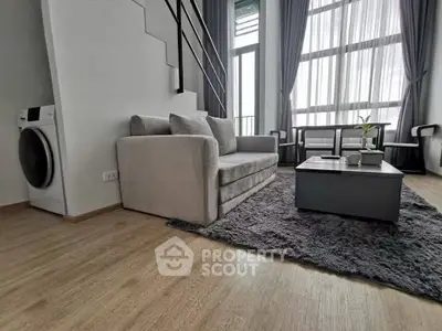 Modern living room with high ceilings and large windows, featuring a cozy sofa and stylish decor.