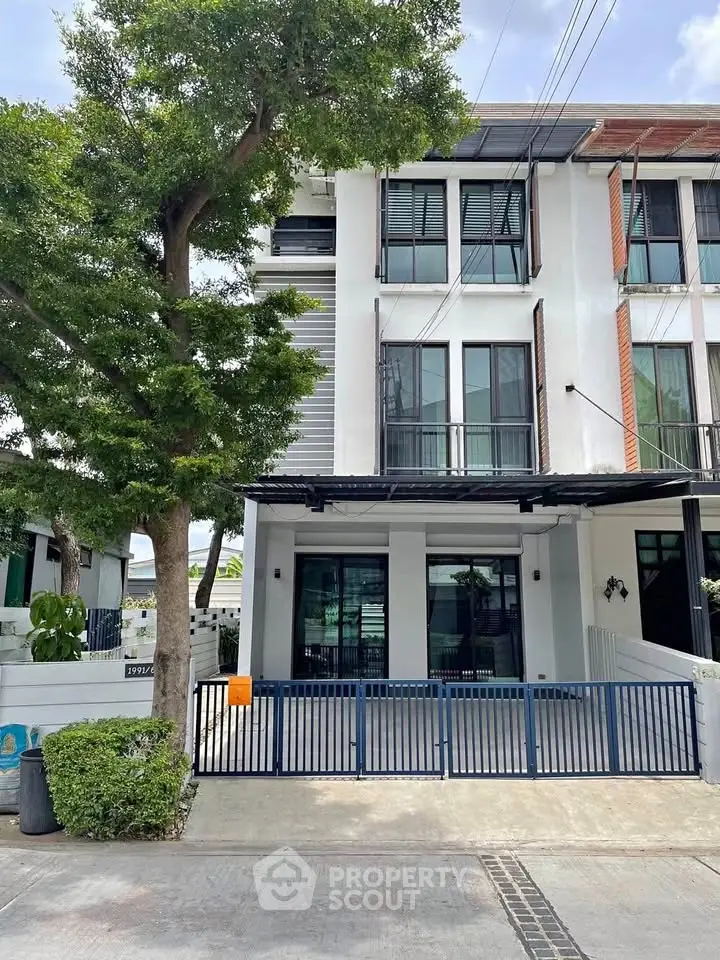 Modern three-story townhouse with gated entrance and lush greenery.