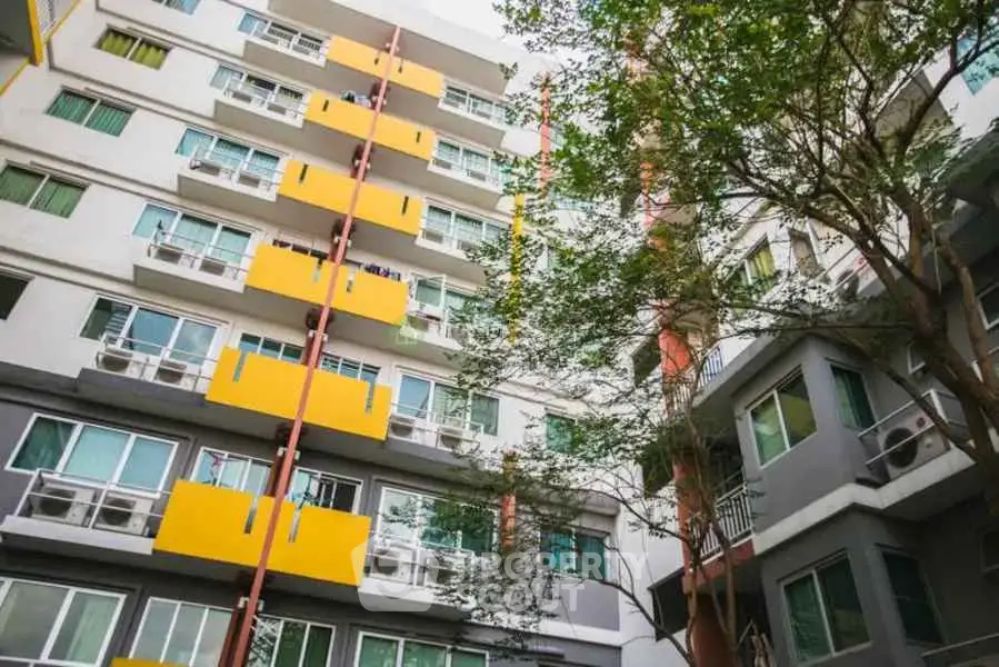 Modern apartment building with vibrant yellow balconies and lush greenery.