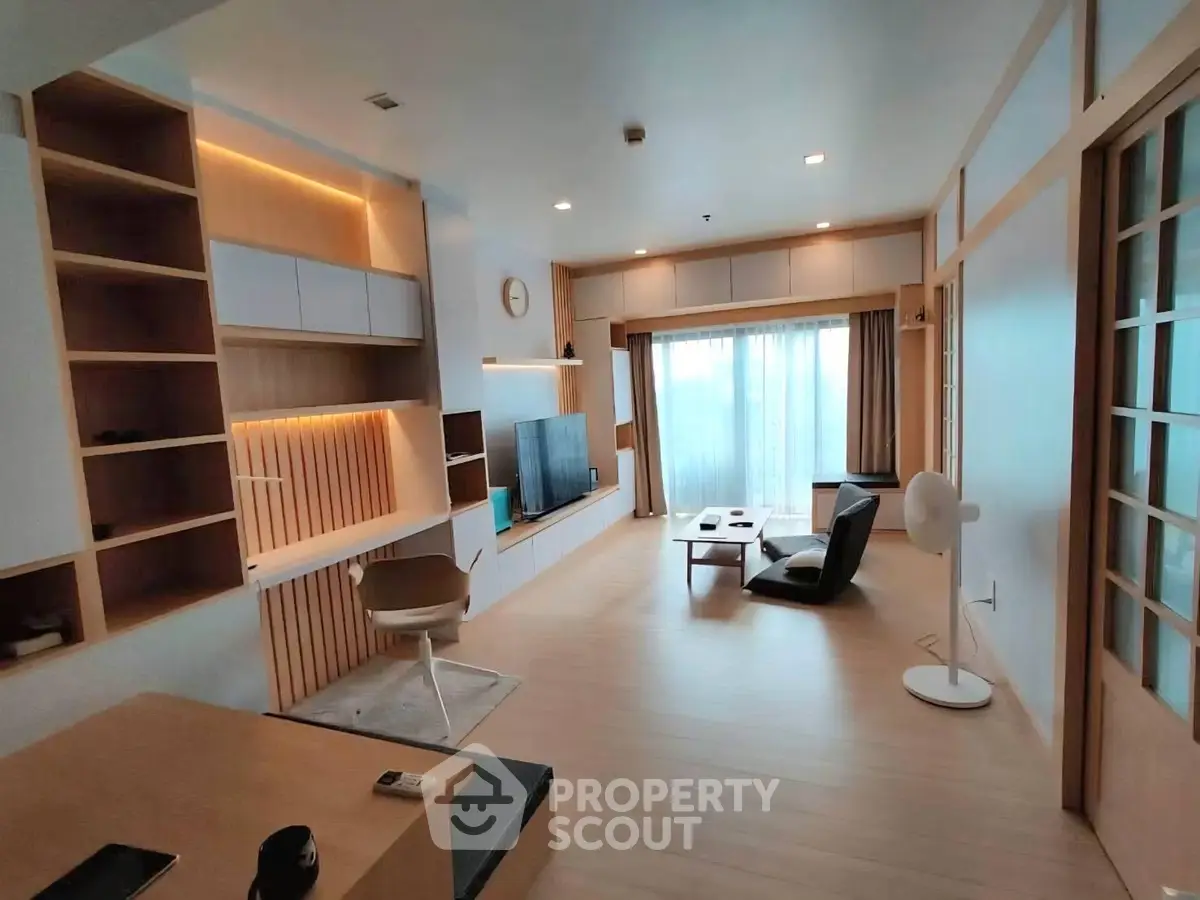 Modern living room with sleek furniture and ambient lighting, featuring a large window and built-in shelving.