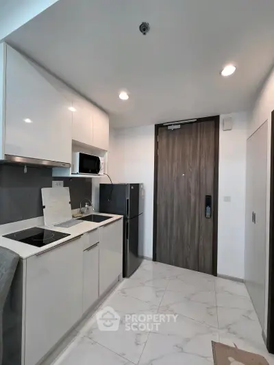 Modern kitchen with sleek white cabinets, built-in microwave, and compact fridge in a stylish apartment.