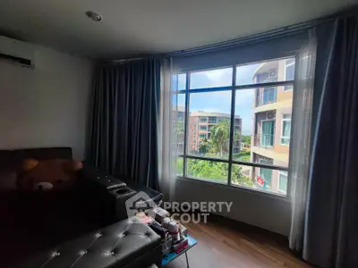 Cozy living room with large window offering a scenic view of modern buildings and lush greenery.